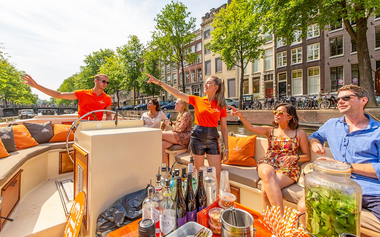 Amsterdam canal cruise with passengers enjoying drinks near Anne Frank House.