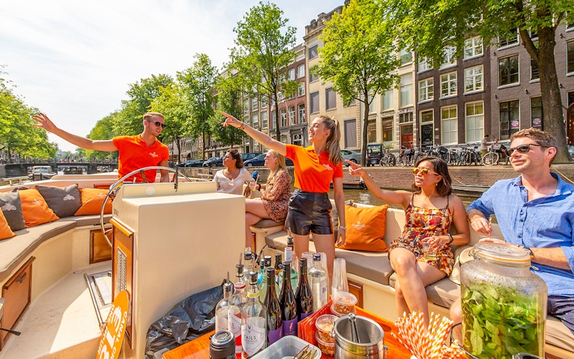 Amsterdam canal cruise with passengers enjoying drinks near Anne Frank House.