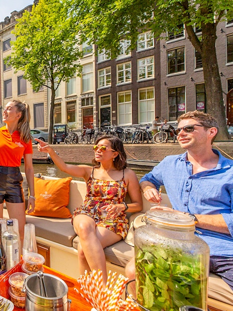 Amsterdam canal cruise with passengers enjoying drinks near Anne Frank House.