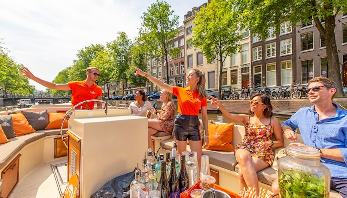 Amsterdam canal cruise with passengers enjoying drinks near Anne Frank House.