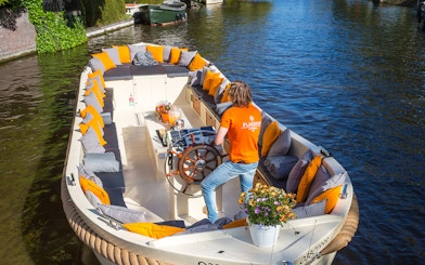 Open boat with seating and flowers cruising Amsterdam canal.