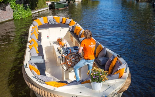 Open boat with seating and flowers cruising Amsterdam canal.