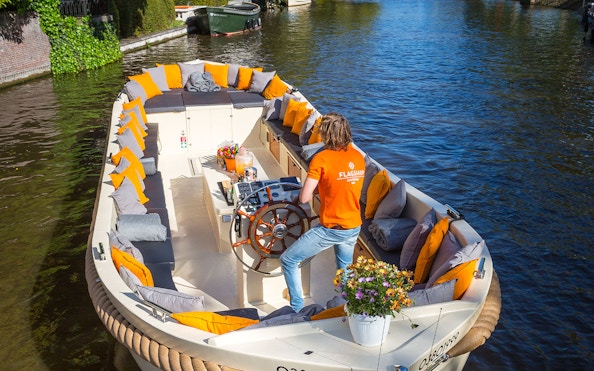 Open boat with seating and flowers cruising Amsterdam canal.