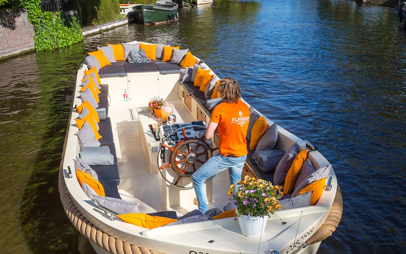 Open boat with seating and flowers cruising Amsterdam canal.