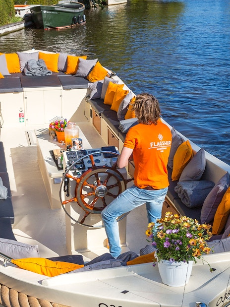 Open boat with seating and flowers cruising Amsterdam canal.