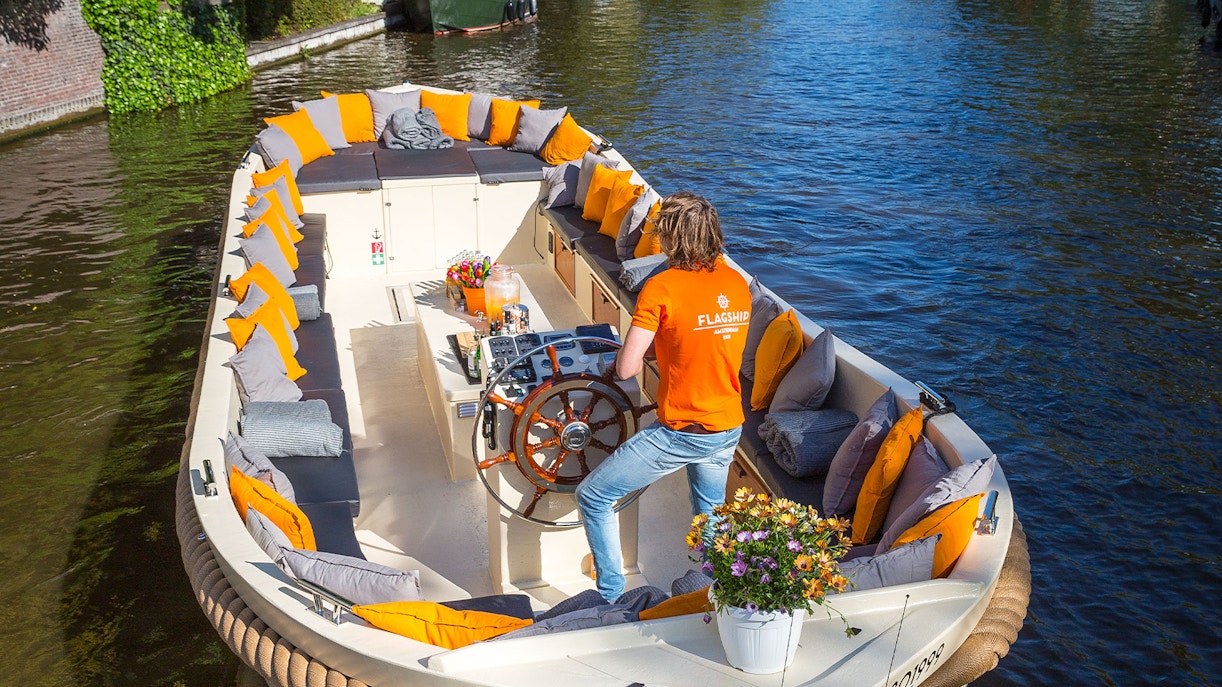 Open boat with seating and flowers cruising Amsterdam canal.