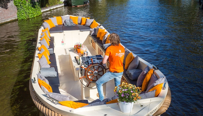 Open boat with seating and flowers cruising Amsterdam canal.