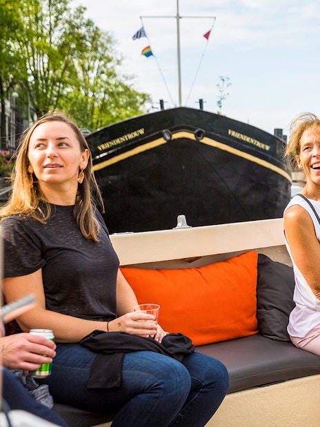 Amsterdam canal cruise with passengers enjoying drinks near Anne Frank House.