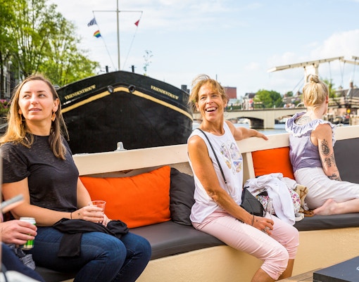 Amsterdam canal cruise with passengers enjoying drinks near Anne Frank House.