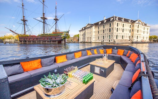 Luxury open boat with drinks cruising Amsterdam canals near historic ship and museum.