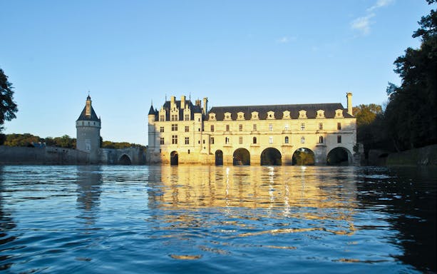 Chenonceau Castle reflecting on the Loire River at sunset.