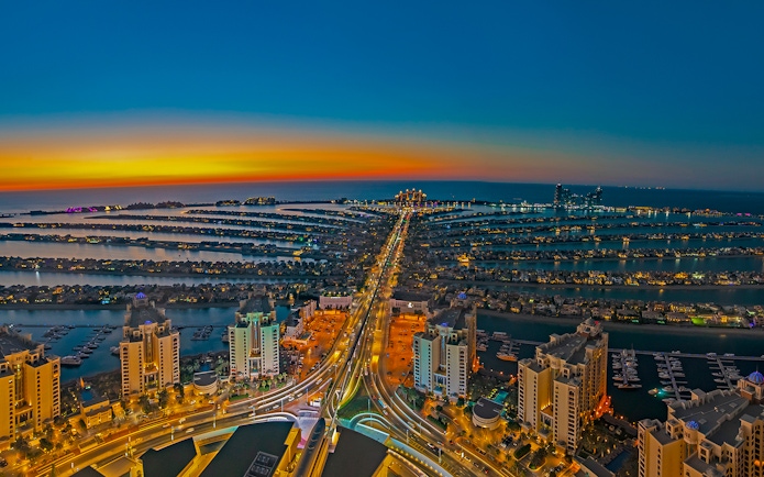 Night view of Palm Jumeirah from the View at the Palm, Dubai, with illuminated buildings and sunset.