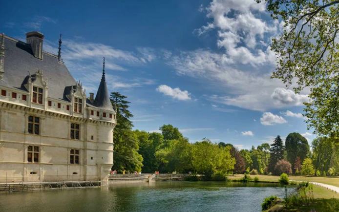 Château d'Azay-le-Rideau by a river with lush greenery and blue sky.
