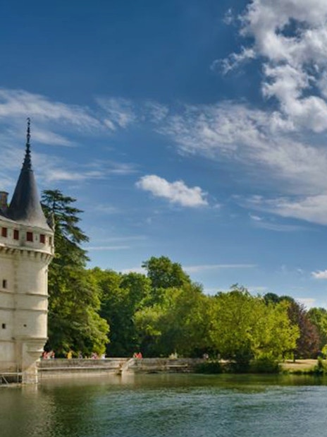 Château d'Azay-le-Rideau by a river with lush greenery and blue sky.