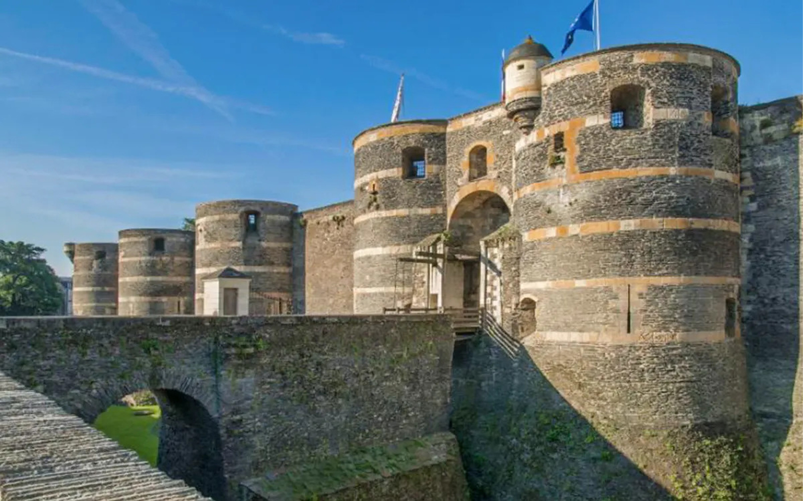 Angers Castle stone towers and entrance bridge under a clear sky.