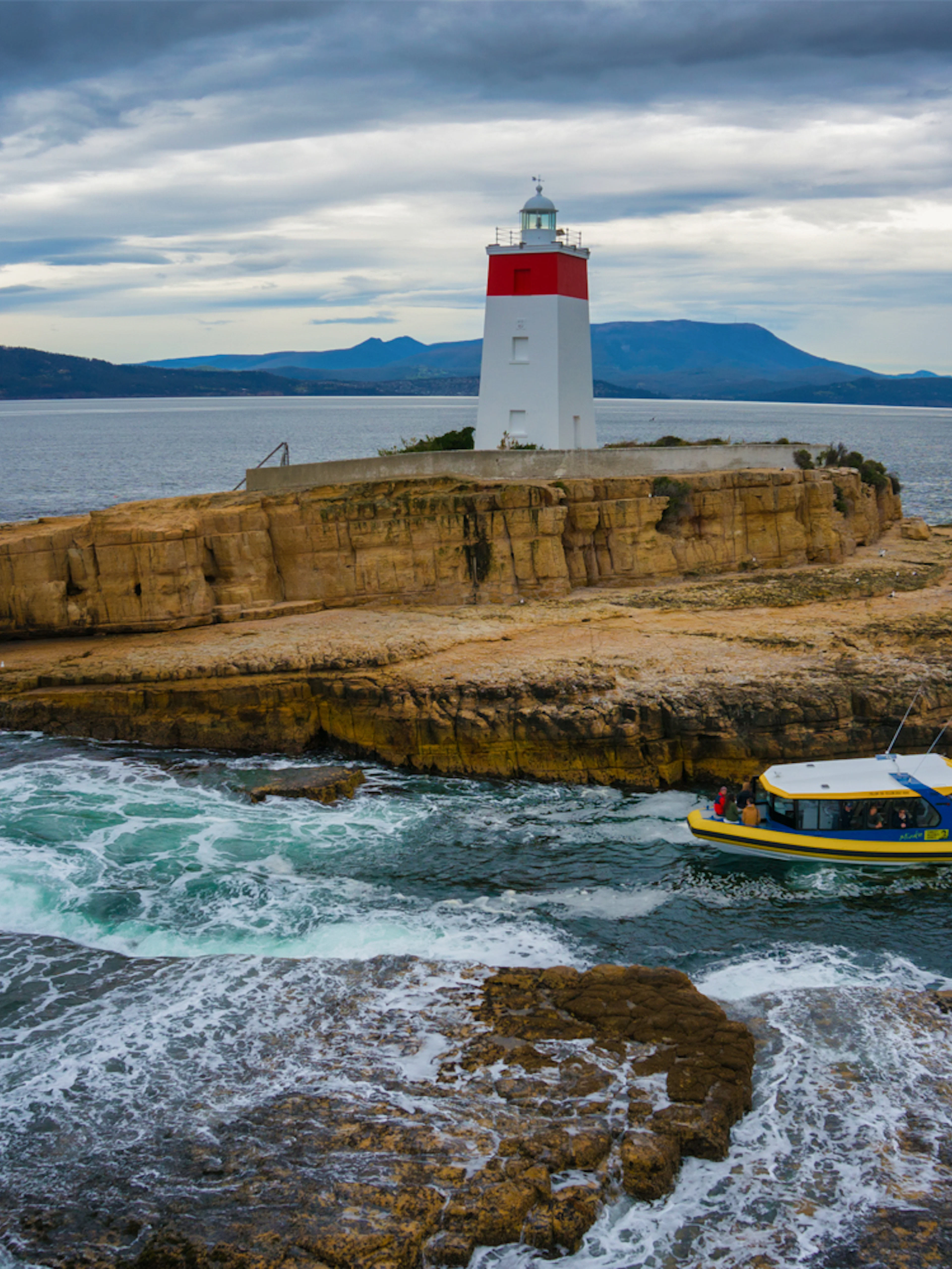 Boat near Iron Pot Lighthouse on rocky island, Tasmania, during Iron Pot Cruise.