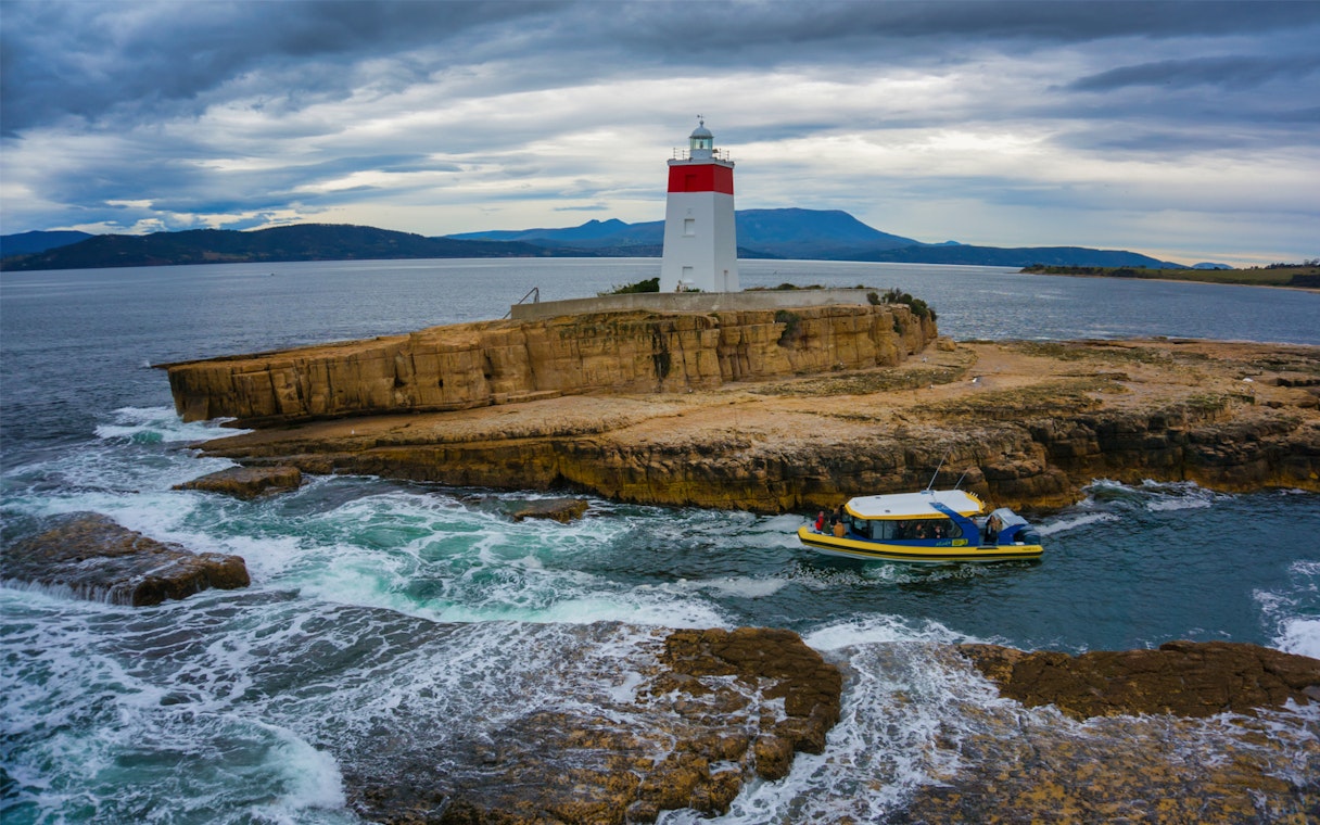 Boat near Iron Pot Lighthouse on rocky island, Tasmania, during Iron Pot Cruise.