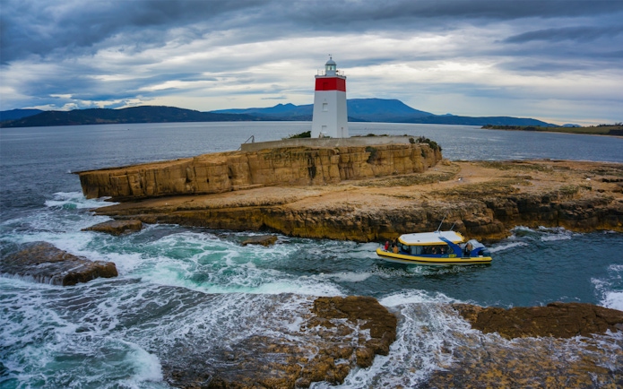 Boat near Iron Pot Lighthouse on rocky island, Tasmania, during Iron Pot Cruise.
