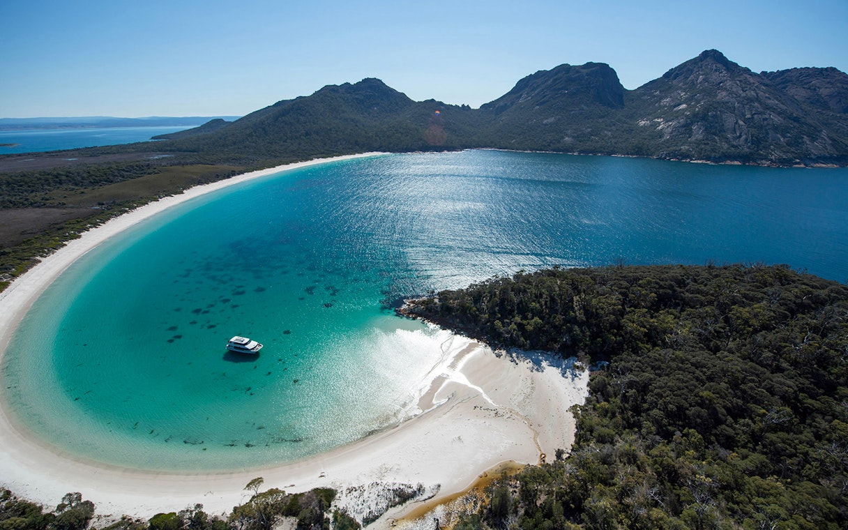 Cruise boat in Wineglass Bay, Tasmania, surrounded by turquoise water and lush hills.