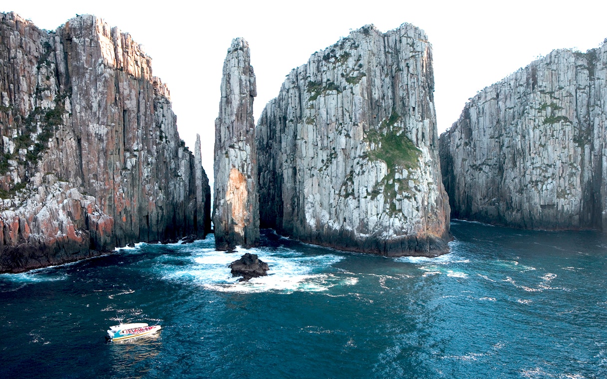 Cruise boat navigating between towering cliffs on Tasman Island, Australia.