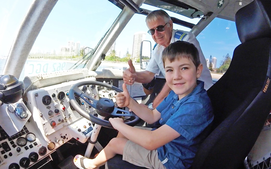 Child and guide giving thumbs up inside Aquaduck vehicle, Sunshine Coast skyline visible.