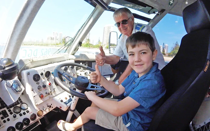 Child and guide giving thumbs up inside Aquaduck vehicle, Sunshine Coast skyline visible.