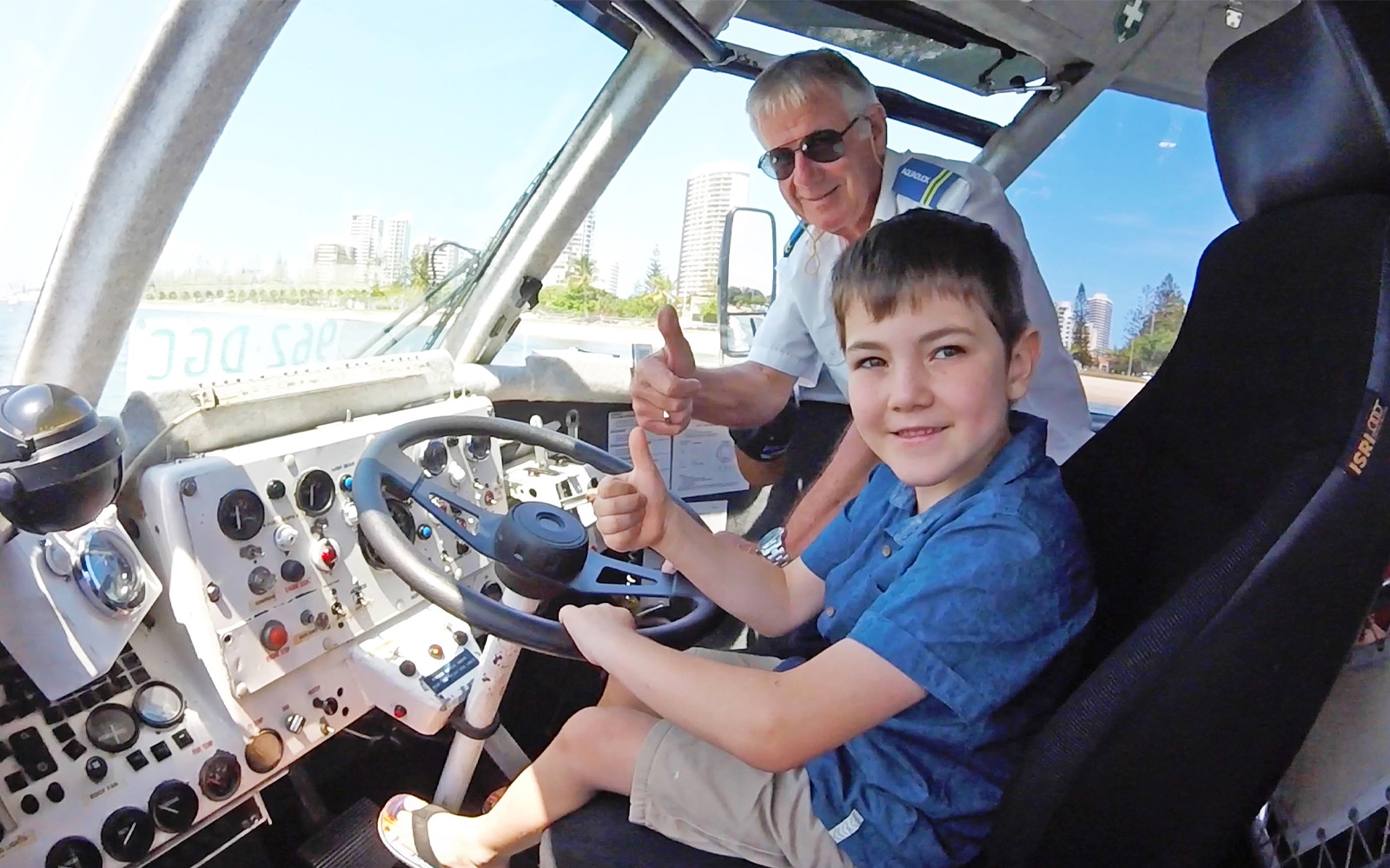 Child and guide giving thumbs up inside Aquaduck vehicle, Sunshine Coast skyline visible.