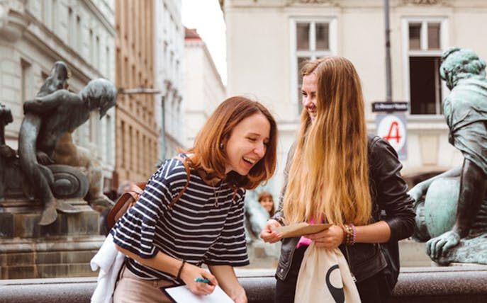 Two women laughing near a fountain with sculptures in Vienna, Austria.