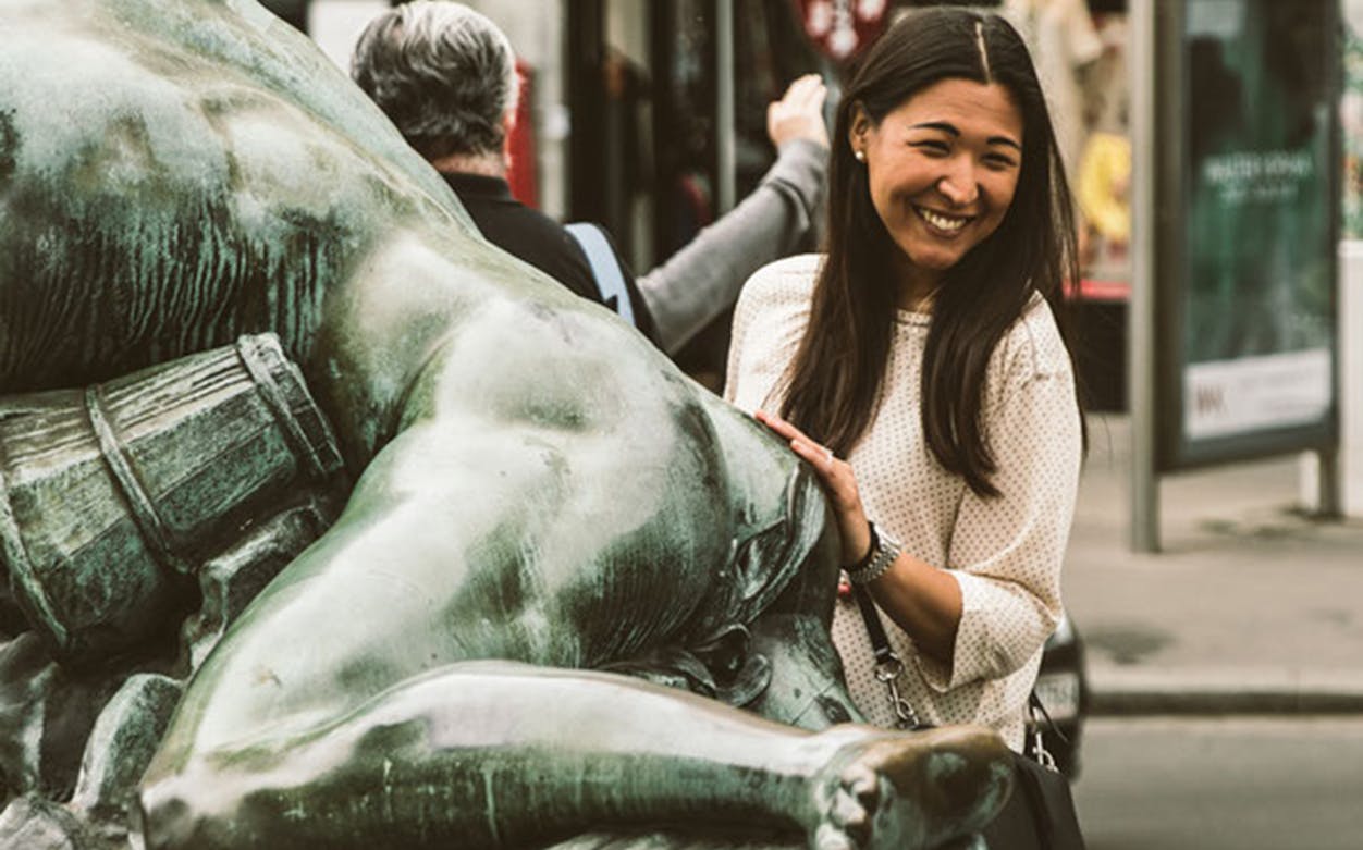Woman smiling beside a bronze statue in Vienna.