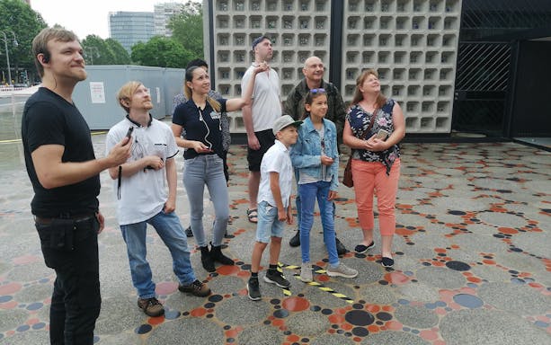 Group of tourists on a Berlin walking tour with audio guides, standing on a patterned pavement.
