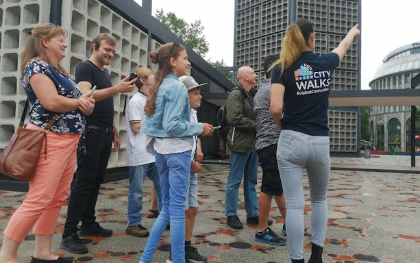 Group of tourists on a guided walking tour in Berlin, listening to a guide near a modern building.