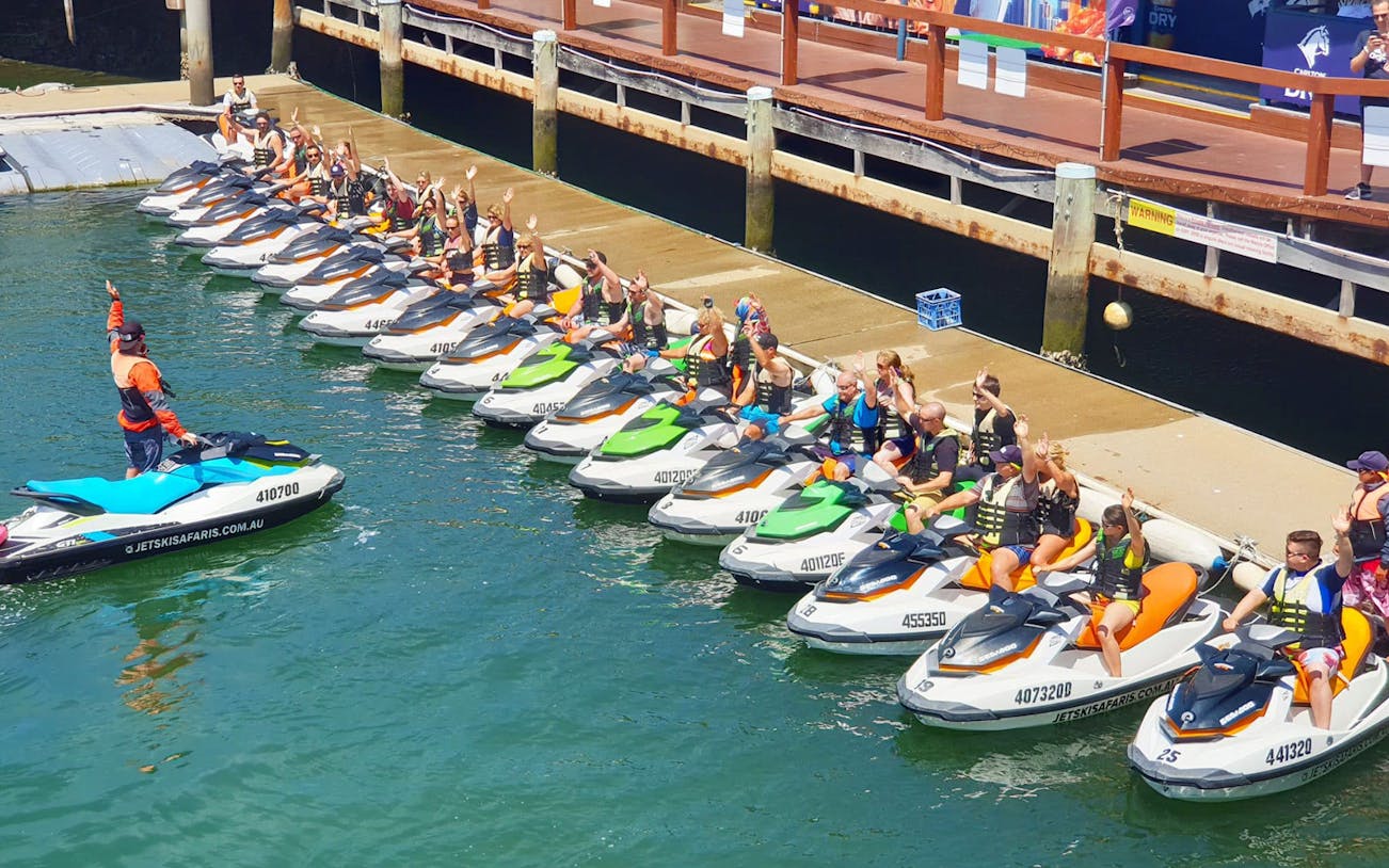 Group preparing for jet ski experience at a dock, wearing life vests, with instructor guiding.
