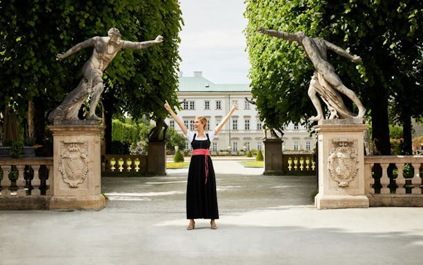 Woman in traditional dress at Mirabell Gardens, Salzburg, between two statues, part of The Sound of Music tour.