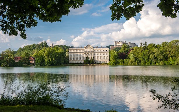 Schloss Leopoldskron and Hohensalzburg Fortress viewed from across a lake in Salzburg.