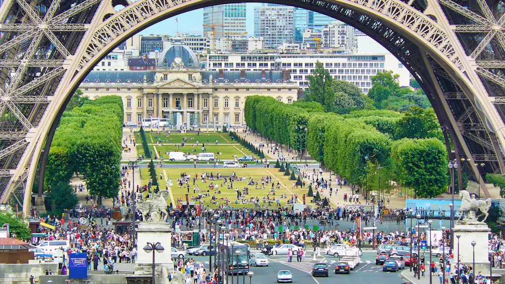 View of Champ de Mars from Eiffel Tower, Paris, with crowds and cityscape in the background.
