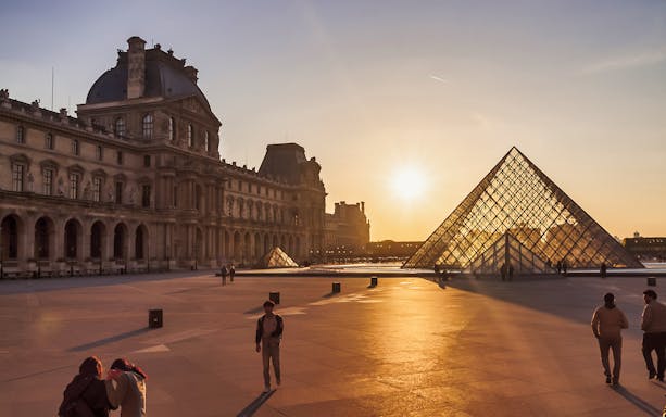 Louvre Museum courtyard with glass pyramid at sunset, Paris.