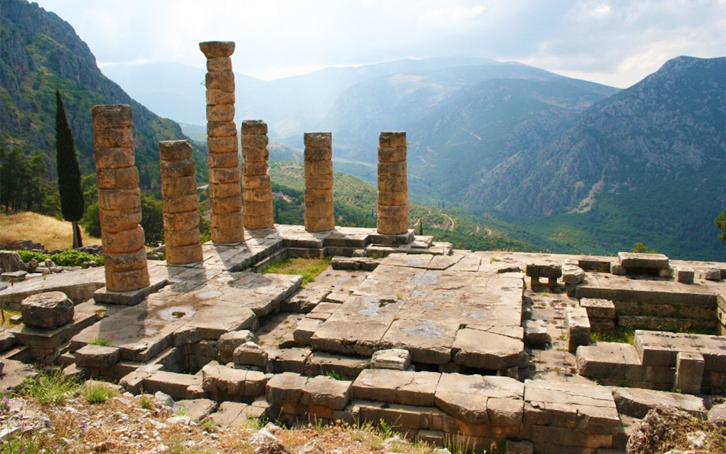 Ancient ruins of the Temple of Apollo at Delphi with mountain backdrop, Greece.