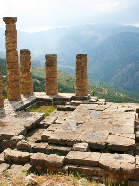 Ancient ruins of the Temple of Apollo at Delphi with mountain backdrop, Greece.