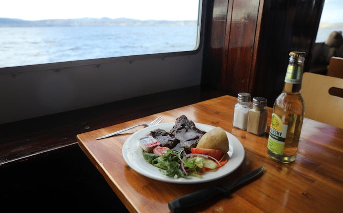 Lunch plate with beef, salad, and potato on a Hobart historic cruise table by the window.