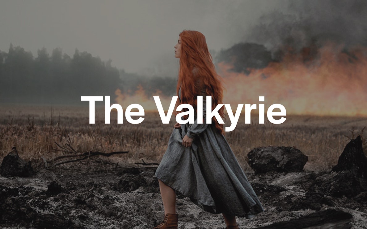 Red-haired woman in medieval dress walking through a smoky, burnt landscape.