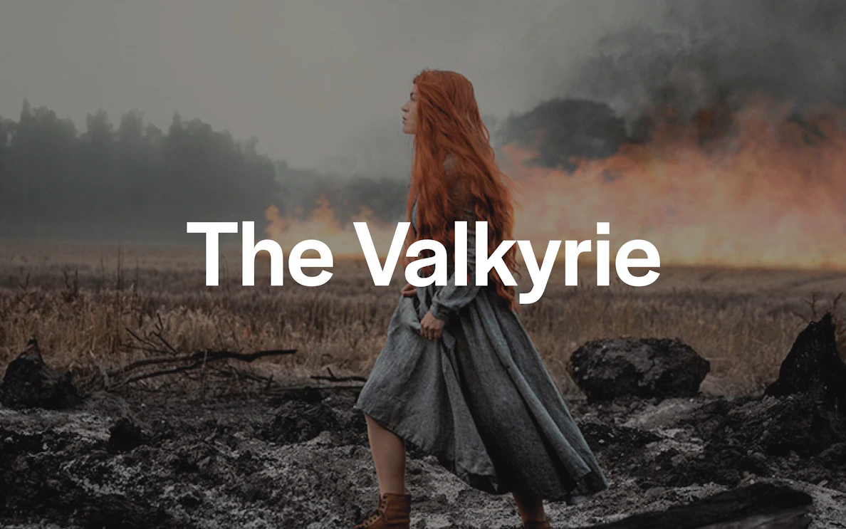 Red-haired woman in medieval dress walking through a smoky, burnt landscape.