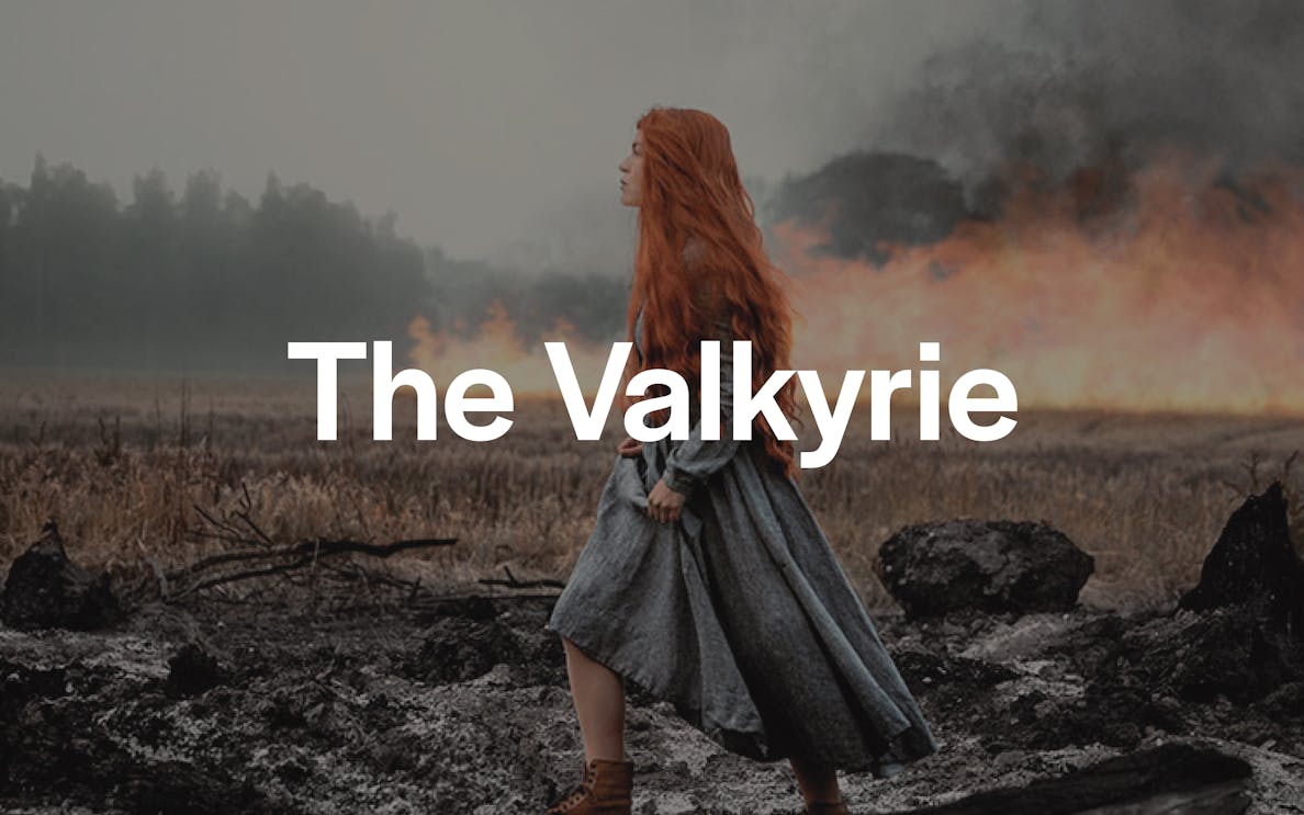 Red-haired woman in medieval dress walking through a smoky, burnt landscape.