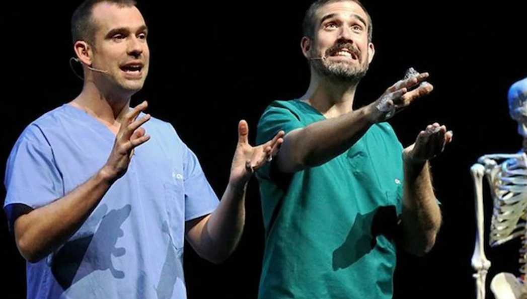 Two presenters in scrubs performing on stage with a skeleton for Operation Ouch Live.