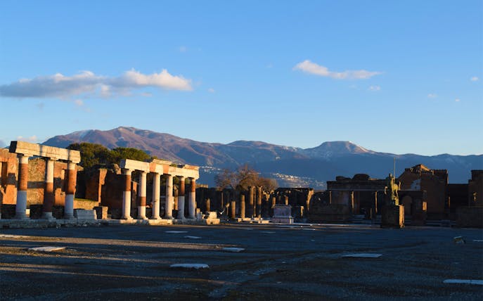Pompeii ruins with columns and mountains in the background, Italy.