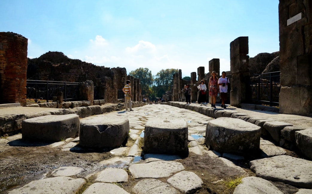 Ancient stone street in Pompeii with tourists exploring, highlighting audioguide service.