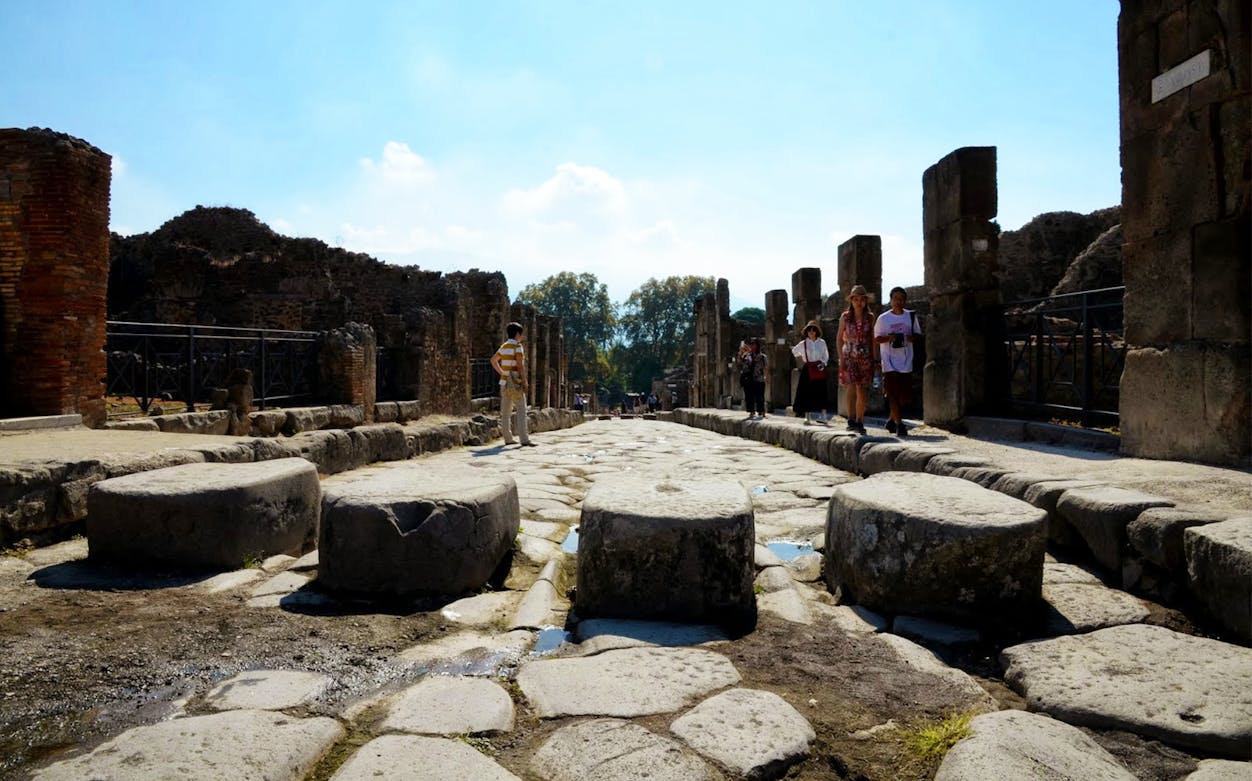 Ancient stone street in Pompeii with tourists exploring, highlighting audioguide service.