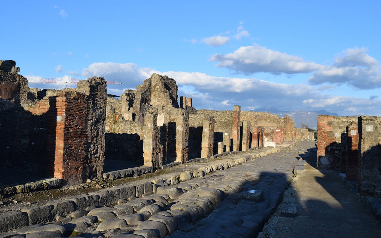 Ancient street in Pompeii with ruins and stone pavement under a clear sky.