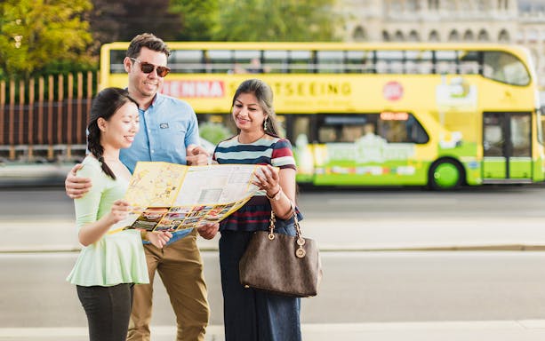 Tourists with a map in front of a yellow hop-on hop-off bus in Vienna.