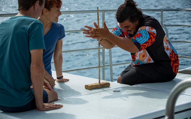 Participants learning traditional fire-starting on Dreamtime Dive & Snorkel tour from Cairns.