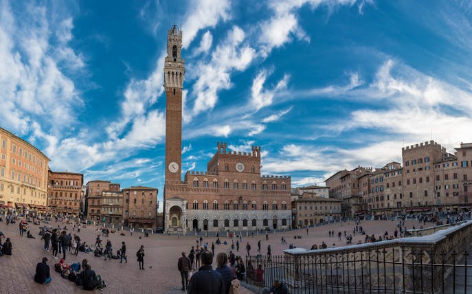 Piazza del Campo in Siena with Torre del Mangia and people walking.